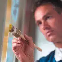 Ein Maler beschichtet ein Fenser mit einem Pinsel.